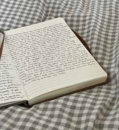 an open notebook sitting on top of a bed covered in checkered sheets and writing