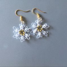 two white and yellow flowers are hanging from gold earwires on a gray surface