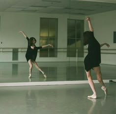 two young women are performing ballet moves in an empty dance studio with mirrors on the wall