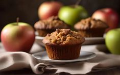 two muffins on a plate with apples in the backgroung behind them