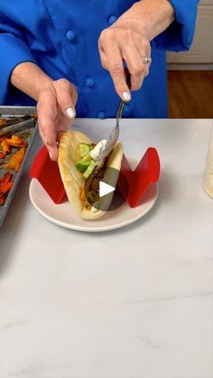 a woman cutting into a taco with a knife and fork on a white plate