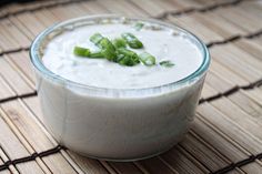 a glass bowl filled with white sauce on top of a bamboo place mat next to a spoon