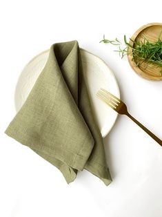 a white plate topped with a green napkin next to a wooden bowl filled with greens