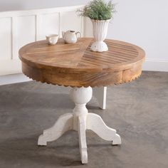 a round wooden table with two white vases on it's legs and a plant in the center