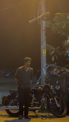 a man standing next to a motorcycle on the side of a road in front of a street light