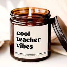 a candle with the words cool teacher vibes on it next to an open book