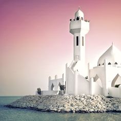 a large white building sitting on top of a rock covered island in the middle of the ocean