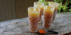 three glasses filled with orange liquid sitting on top of a wooden table next to an orange peel