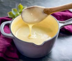 a wooden spoon is being used to dip cheese into a sauce in a pot on a purple cloth