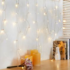 some candles are sitting on a table near a wall with white lights and a book