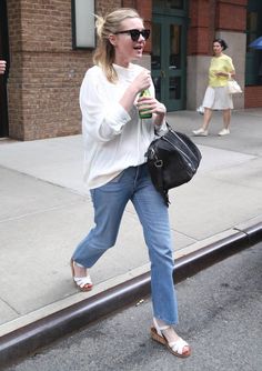 a woman is walking down the street with her handbag and coffee in her other hand