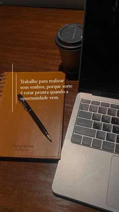 an open notebook sitting on top of a wooden desk next to a laptop and coffee cup