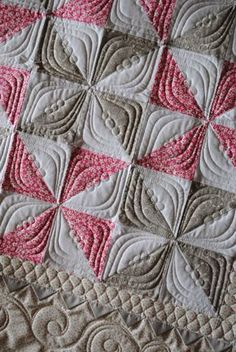 a close up of a quilt on a bed with pink and gray squares in the center