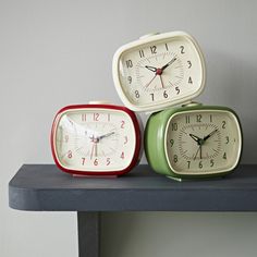 three small clocks sitting on top of a shelf next to each other, one red and one green