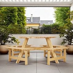 a wooden picnic table sitting on top of a cement floor next to potted plants