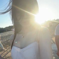 a woman standing on top of a sandy beach next to the ocean with sun shining through her hair