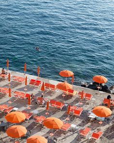 many orange umbrellas and chairs near the water