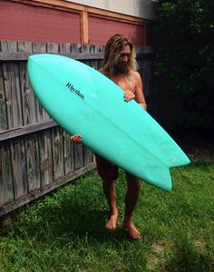 a man holding a blue surfboard in his right hand while standing next to a wooden fence