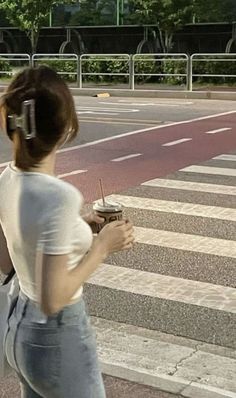 a woman walking across a cross walk holding a cupcake in her hand and a cell phone to her ear