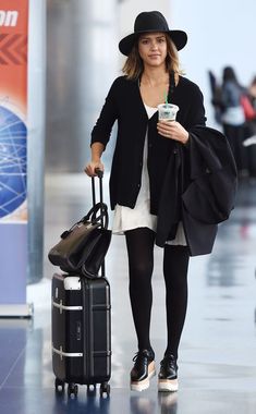 a woman walking through an airport with her suitcase and coffee cup in one hand while holding the other