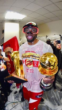 a man holding two golden trophies in his hands and wearing goggles on his face