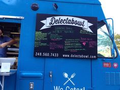 a man standing in the doorway of a blue food truck with a menu on it's side