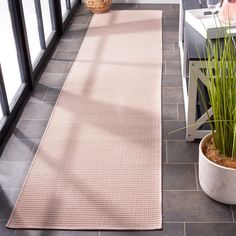 a pink rug is on the floor next to a potted plant and glass windows