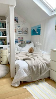 a white bed sitting under a skylight in a bedroom next to a book shelf