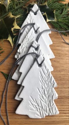 three white ceramic christmas trees are sitting on a wooden table next to evergreen leaves and twine