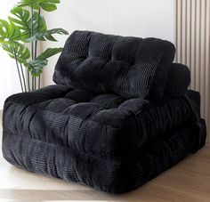 a black recliner sitting on top of a hard wood floor next to a green plant