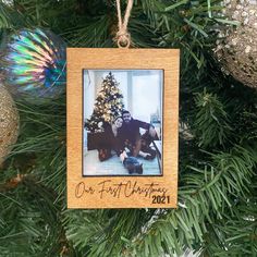 an ornament hanging on a christmas tree with ornaments around it and a photo of two people