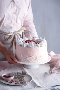 a woman is holding a pink cake with white frosting on it and there is a fork in front of the cake