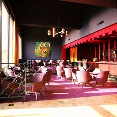 an empty restaurant with pink chairs and purple carpeted flooring in front of a large painting on the wall