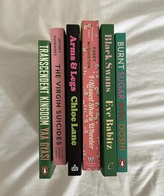 four books are lined up on a white sheet, one is green and the other is pink