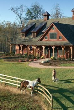 two horses are standing in front of a large house with a wooden fence and green grass