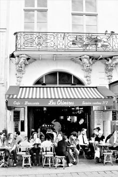 black and white photograph of people sitting at tables in front of a restaurant