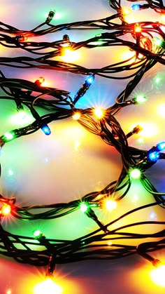 multicolored christmas lights are arranged on a white surface with blue and pink background