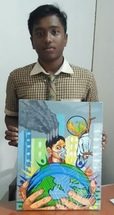 a young man holding up a painting on top of a table