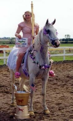 a woman riding on the back of a white horse next to a bucket filled with flowers