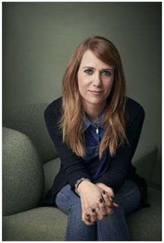 a woman sitting on top of a green couch with her hands crossed and looking at the camera