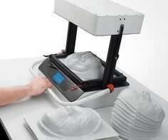 a person is using a machine to make white plates on a table with their hands