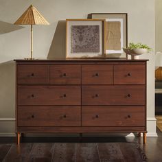 a wooden dresser with two lamps and pictures on top