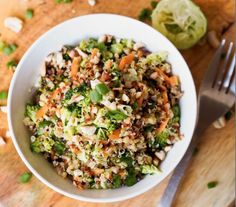 a white bowl filled with broccoli, carrots and other food on top of a wooden table