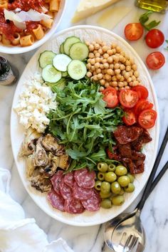 two bowls filled with different types of food on top of a white table next to utensils