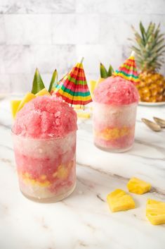 two glasses filled with ice cream and pineapple slices on a marble counter top next to plates of pineapples