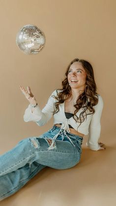 a woman is sitting on the floor and throwing a disco ball up in the air