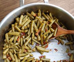 green beans are being cooked in a pot with a wooden spoon on the side and bacon