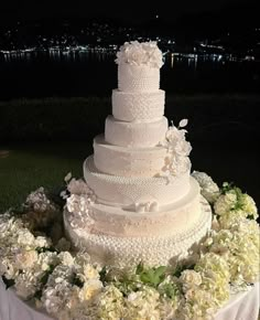 a wedding cake with white flowers and greenery on the table in front of water