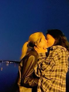 two people standing next to each other near the water and one person is kissing the other