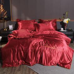 a woman laying on top of a bed covered in red sheets and satin materials